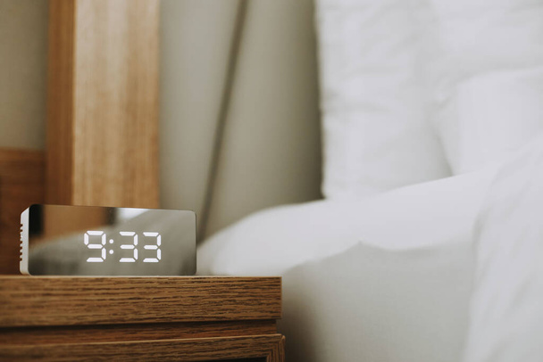 A shot of a smart alarm on a wooden surface near the bed on a blurry background - Foto, afbeelding