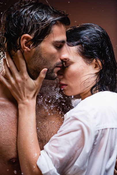 woman in white shirt touching shirtless man near water splashes on dark background - Foto, imagen