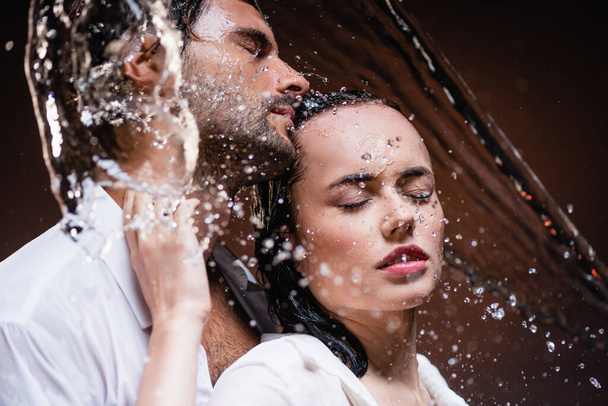 wet man and woman standing with closed eyes near water splashes on dark background - Fotografie, Obrázek
