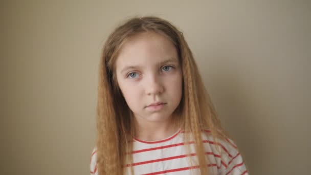Kis fáradt lány hosszú szőke hajjal, pózol a kamerának, és egyik oldalról a másikra lóbálja a testét a szobában. Kis unatkozó gyermek portréja a bézs fal hátterében. Lezárás Lassú mozgás - Felvétel, videó