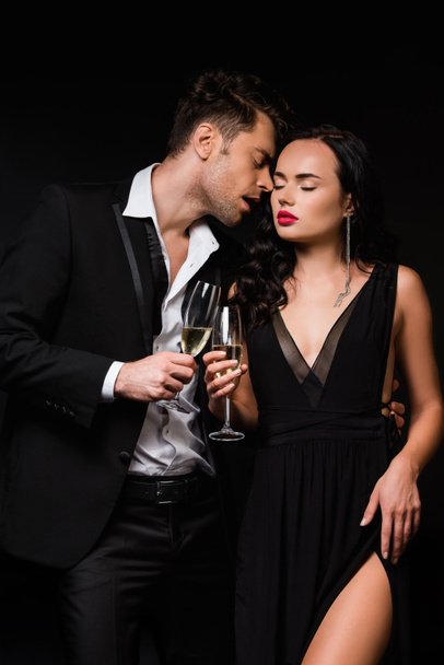 sexy couple holding glasses of champagne and clinking isolated on black  - Photo, Image