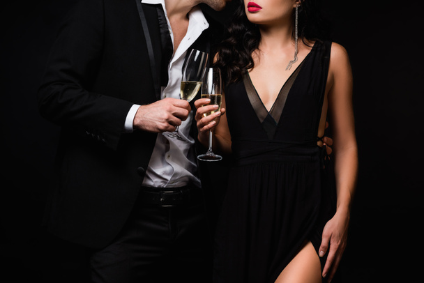 cropped view of sexy couple holding glasses of champagne while toasting isolated on black - Fotó, kép