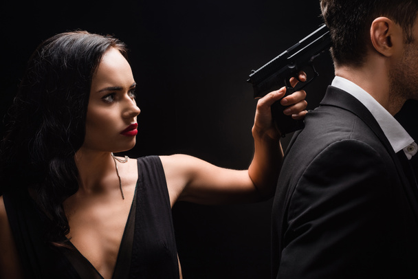 dangerous woman in dress holding gun near man in suit isolated on black  - 写真・画像