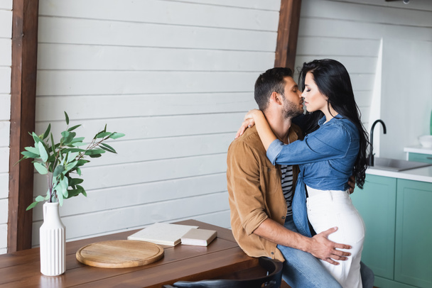 young couple in stylish casual clothes kissing in kitchen near table - Foto, Imagem