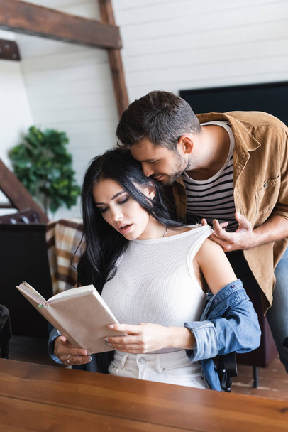 jeune homme séduire sexy brunette copine lecture livre à la maison - Photo, image