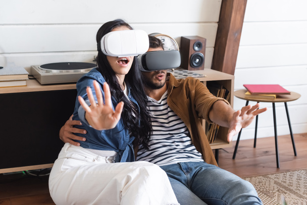 excited couple gesturing while gaming in vr headsets on floor at home - Fotografie, Obrázek