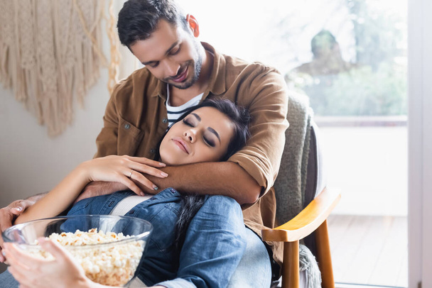 happy man embracing girlfriend holding bowl of popcorn with closed eyes - Foto, afbeelding