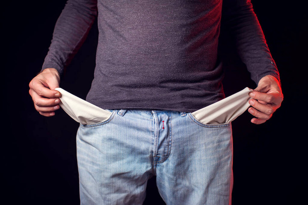 Muž ukazuje prázdnou kapsu džínů před černým pozadím. Koncept chudoby a finančních problémů - Fotografie, Obrázek