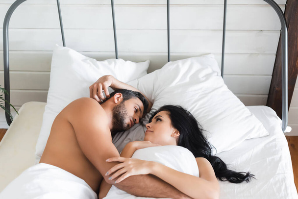 pareja joven mirándose mientras yacen en la cama bajo una manta - Foto, imagen