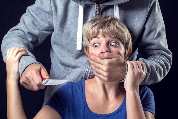 Man in hooded sweater covering a woman'smouth and holds a knife. Concept of violence or kidnapping.  - Fotoğraf, Görsel