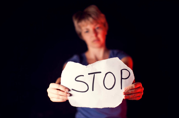 Жінка тримає папір з повідомленням, щоб допомогти їй перед чорним фоном. Люди, насилля в родині, злочинність - Фото, зображення