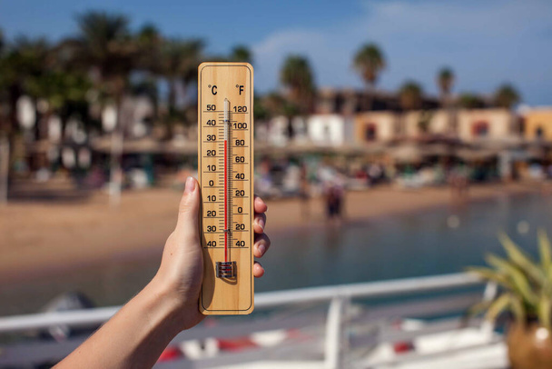 Hand of woman holds thermometer at beach background. Summer, climate and weather concept - Fotoğraf, Görsel