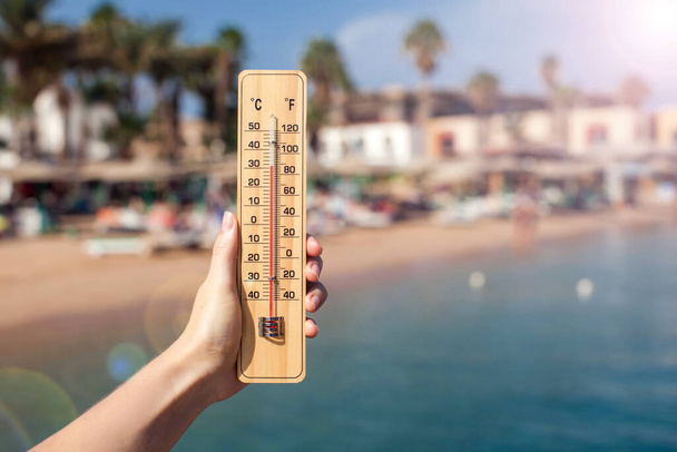Hand of woman holds thermometer at beach background. Summer, climate and weather concept - Фото, изображение