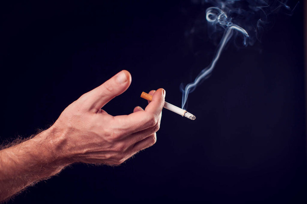 Сигарета в руке на черном фоне. Концепция дымовой зависимости - Фото, изображение
