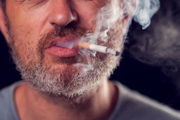 Ein Porträt des Mannes raucht Zigarette auf schwarzem Hintergrund. Konzept zur Tabakabhängigkeit - Foto, Bild