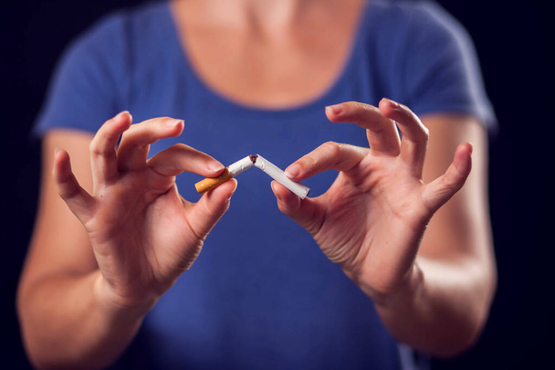 Elinde kırık sigara tutan mavi tişörtlü bir kadın. Sigara içmeyi bırak - Fotoğraf, Görsel