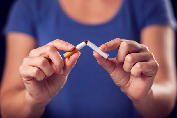 Nainen sinisessä t-paidassa pitelee rikkinäistä savuketta käsissään. Lopeta tupakointi käsite - Valokuva, kuva