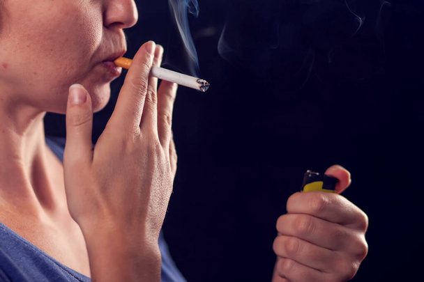 Woman smokes cigarette on black background. Tobacco addiction concept - Photo, Image