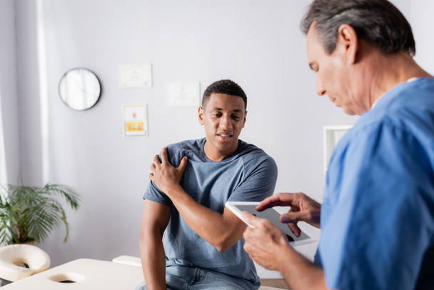 Afrikkalainen amerikkalainen potilas kärsii kipua lähellä lääkäri digitaalinen tabletti  - Valokuva, kuva