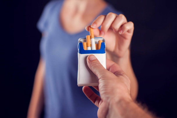 Woman takes cigarette on black background. Tobacco addiction concept - Photo, Image