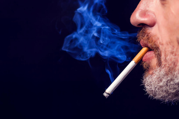 Un retrato del hombre fuma cigarrillos sobre fondo negro. Concepto de adicción al tabaco - Foto, imagen