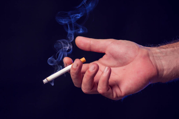 黒の背景に手にタバコ。煙中毒の概念 - 写真・画像