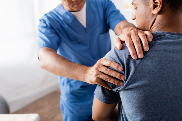 chiropractor werken met gewonde arm van Afrikaanse Amerikaanse patiënt op wazige voorgrond - Foto, afbeelding