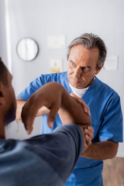 doctor trabajando con lesionado afroamericano hombre en borrosa primer plano  - Foto, Imagen