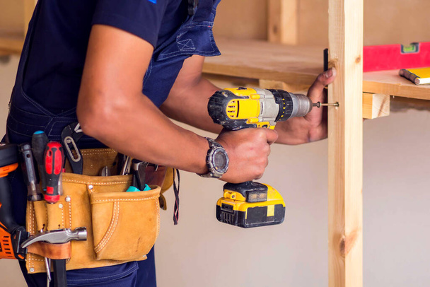 Handyman with yellow headphones works with drill does repair. - Photo, Image