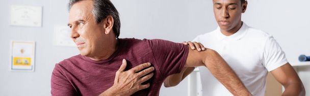 Afrikaans-Amerikaanse fysiotherapeut werkt met volwassen man in kliniek, banner - Foto, afbeelding