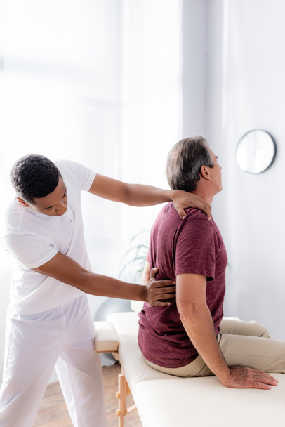 chiropratico afroamericano che lavora con la schiena di uomo di mezza età in clinica - Foto, immagini