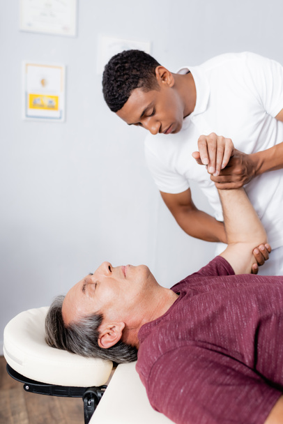Afrikaans amerikaanse chiropractor corrigeren arm van middelbare leeftijd man in kliniek - Foto, afbeelding