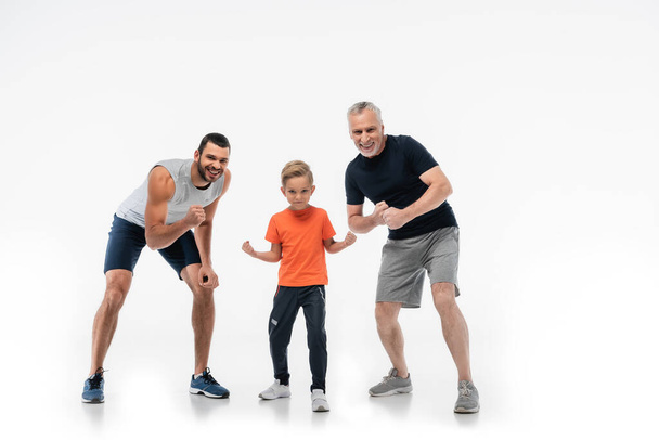 garçon avec papa et grand-père en vêtements de sport démontrant la force tout en souriant à la caméra sur blanc - Photo, image