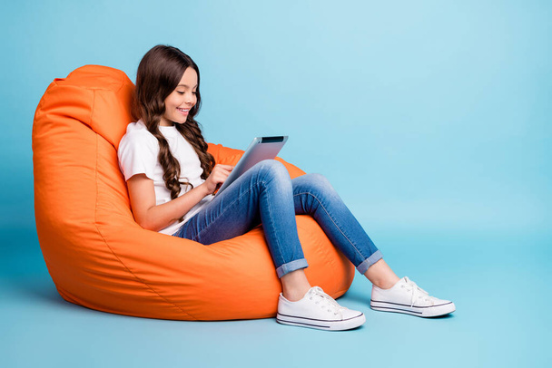 Portrait of nice attractive cheerful cheery focused wavy-haired girl sitting in chair using tablet ebook isolated on bright vivid shine vibrant blue teal turquoise color background - Fotografie, Obrázek