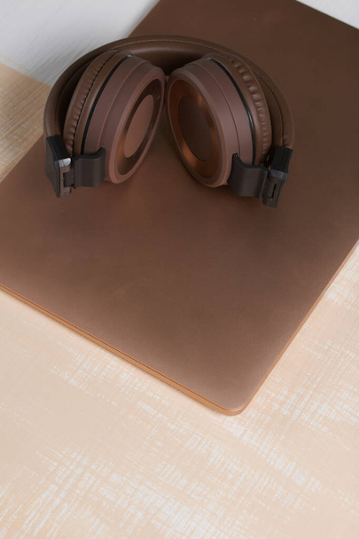 Fragment of a pink notebook. Nearby are wireless headphones in brown. The surface is painted in white and beige. - Фото, изображение