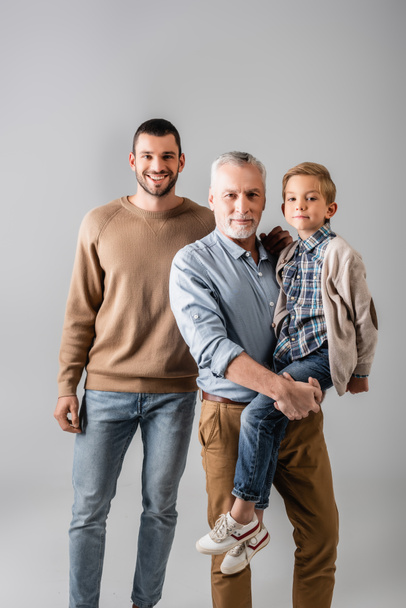 happy mature man holding grandson near cheerful son isolated on grey - Photo, Image