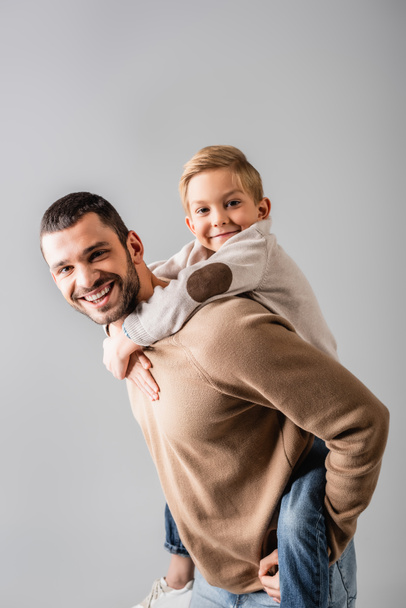 happy man piggybacking smiling son while looking at camera together isolated on grey - Zdjęcie, obraz