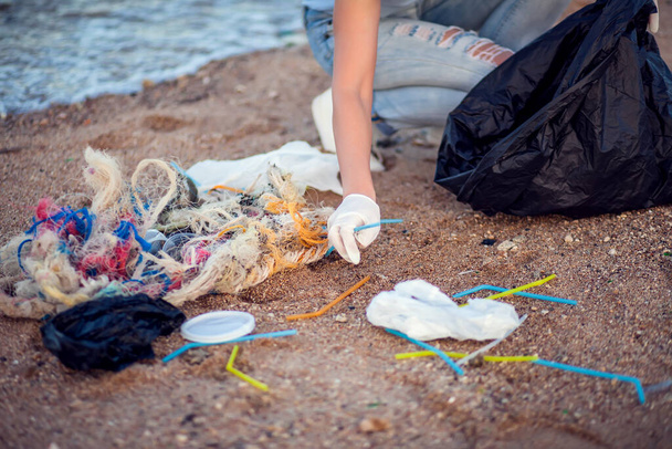 Жінка в синій сорочці з білими рукавичками і великим чорним пакетом, що збирає сміття на пляжі. Концепція захисту навколишнього середовища та забруднення планети
 - Фото, зображення