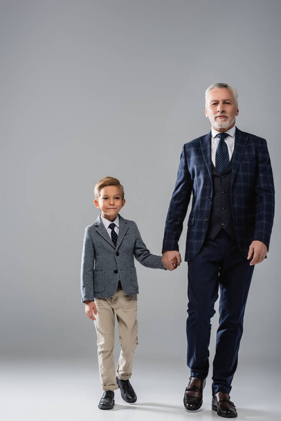 mature businessman holding hand of grandson while walking on grey - Foto, imagen