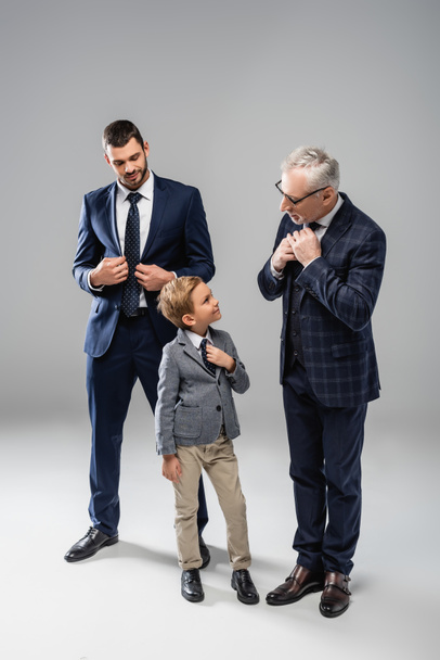 smiling businessman looking at grandfather and grandson touching ties on grey - Φωτογραφία, εικόνα