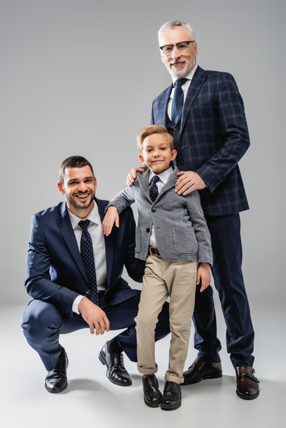 happy businessmen with boy in formal wear smiling at camera on grey - Foto, Imagem