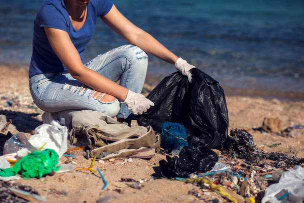 Femme bénévole avec sac noir ramasser les ordures sur la plage. Concept de pollution environnementale - Photo, image