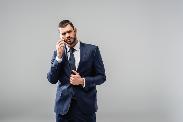thoughtful businessman in suit talking on mobile phone isolated on grey - Foto, Bild