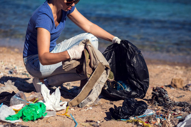 Donna volontaria con borsa nera raccogliere spazzatura sulla spiaggia. Concetto inquinamento ambientale - Foto, immagini