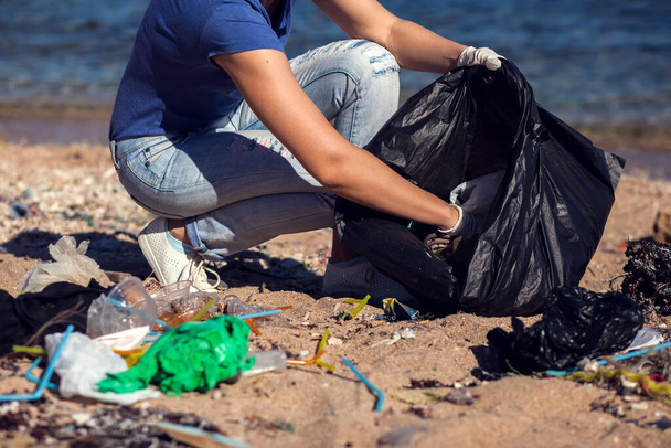 Mujer voluntaria con bolsa negra recoge basura en la playa. Concepto de contaminación ambiental - Foto, Imagen