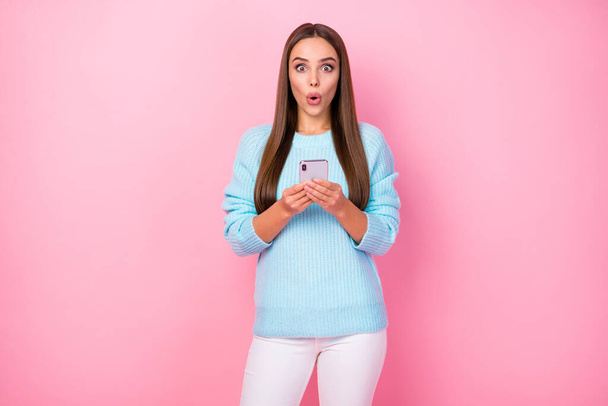 Photo of pretty shocked lady hold telephone check followers enjoy many repost like comments wear knitted blue sweater white trousers isolated pastel pink color background - Foto, imagen