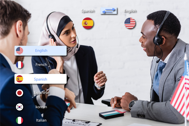 interraciale zakenpartners in headsets in de buurt van digitale vertaler op wazige voorgrond, vertaling applicatie interface illustratie - Foto, afbeelding
