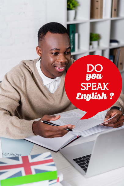 ευτυχής αφρικανός αμερικανός διερμηνέας που εργάζεται κοντά στο lap-top σε θολό προσκήνιο, φυσαλίδα λόγου με μιλάτε αγγλικά εικονογράφηση ερώτηση - Φωτογραφία, εικόνα