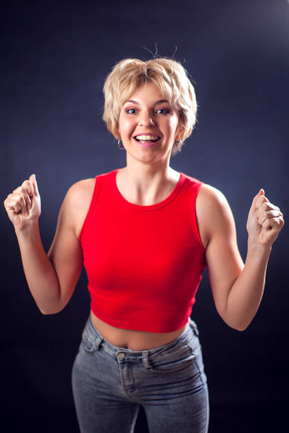 A portrait of happy young woman with short blond hair in red shirt in front of black background. People, emotions and beauty concept - Photo, Image