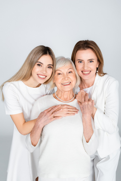 drie generatie van gelukkige vrouwen glimlachen terwijl kijken naar camera geïsoleerd op grijs - Foto, afbeelding